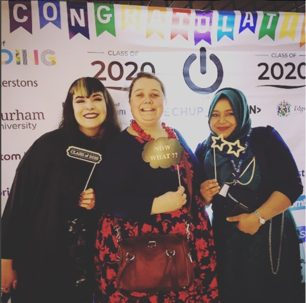 Picture of three women in front of a TechUPWomen Graduation backdrop holding props