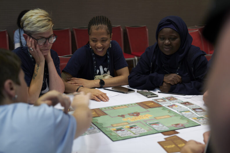 Image shows a group of women sat around a board game on a table.